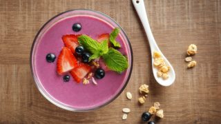 紫色冰沙与木质表面草莓和黑葡萄的扁平式敷设拍旁边的勺子和一些坚果