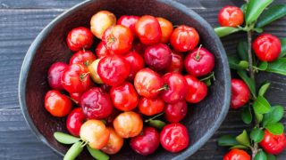 木桌上放着一碗新鲜的红针叶樱桃和树叶