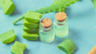 芦荟叶片,叶片切片,和两个瓶子与油旁边的蓝色背景