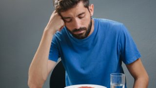 一名看起来沮丧的男子低头盯着面前一杯水旁边放着的一盘食物