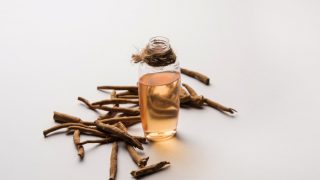 一瓶ashwagandha油保存在古老的草药旁边,背景是白色的