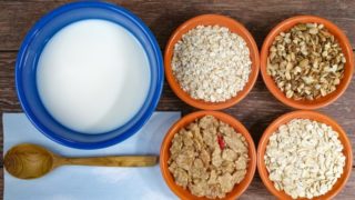 不同种类的麦片放在碗里,旁边是一碗牛奶和一个木勺