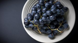 一个白色的碗紫色的葡萄在漆黑的计数器