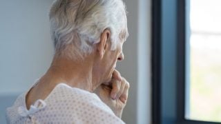 一位老人坐在医院长袍望着窗外