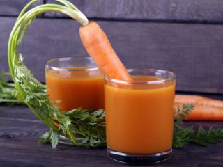 carrotjuice 一个胡萝卜从放在黑色桌子上的两杯胡萝卜汁中的一杯中伸出来