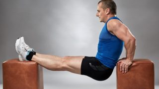 一个穿着运动服的男人正在两个棕色凳子之间做俯冲动作。