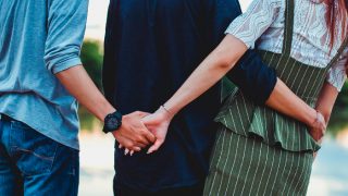 两个男孩和一个女孩在后面咔哒一声。中间的男孩用胳膊搂着女孩的腰,而另一个男孩在背后拉着女孩的手。
