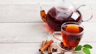 白色木桌上放着水壶和一杯肉桂茶,茶里有肉桂棒和八角