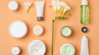 瓶子,罐子,和浴缸包含护肤配方连同在一个桃子的背景上的花。