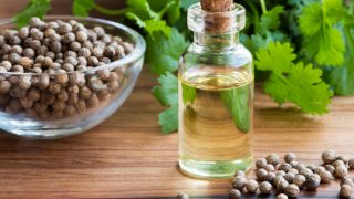 一瓶香菜油,木桌上有一碗香菜籽和叶子