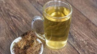 一杯玉米丝茶放在一捆玉米丝旁边,放在一个木制平台上