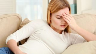 一位孕妇坐在沙发上,抱着头,看上去很紧张