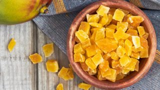 一个木碗,里面放着干芒果片和一个完整的新鲜芒果,放在木桌上