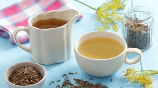 一个白色的杯子和一个装满茴香茶的罐子,一个碗和一盒茴香种子放在木桌上