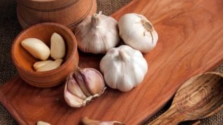 将切成片的大蒜、大蒜丁香、大蒜鳞茎放在砧板上的木碗中