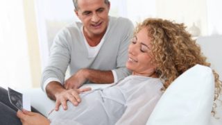 一位年长的孕妇在看超声波图像时微笑着,一位年长的男人把手放在女人的肚子上。