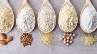 各种各样的无麸质面粉放在木制的勺子和灰色的柜台上