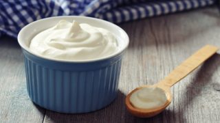 酸奶放在蓝色的碗里,旁边放着酸奶木勺