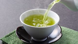 绿色的垫子上放着一个白色的杯子,从茶壶里倒出绿茶