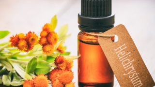 一小瓶蜡菊精华油与蜡菊鲜花上一张木桌