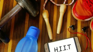 屏幕上显示HIIT的手机放在桌子上,旁边是耳机、水瓶、哑铃、鞋子和跳绳