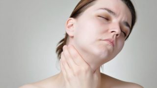一位年轻女子拿着从她的甲亢痛苦的喉咙痛苦