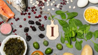 一张手拿着写着“我”的卡片的平线照片,在蓝色的表面上,周围是干果、水果、鱼、绿色蔬菜、鸡蛋、海藻和盐。