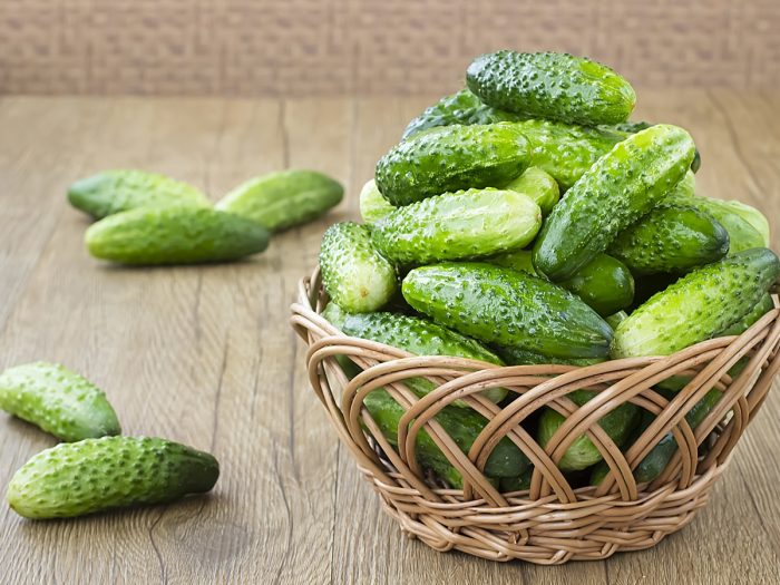 A basket filled with fresh green cucumbers on a wooden table