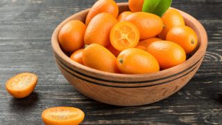 一碗放在深色桌子上的整块和对半块的金橘