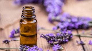 木桌上薰衣草枝旁边放着一瓶玻璃瓶薰衣草精油