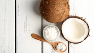 一个小的玻璃瓶&填充有固化椰子油匙的顶视图,毗邻2个椰子在白色背景