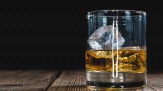 一块玻璃与麦芽酒和冰在它的木桌上面