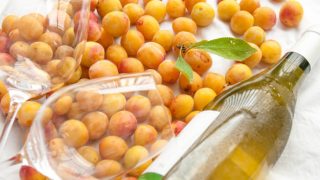 两个酒杯和一个玻璃瓶放置在李子的床。