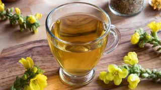 Mullein茶在一个玻璃杯子保持在一个木制平台上,在Mullein花旁边