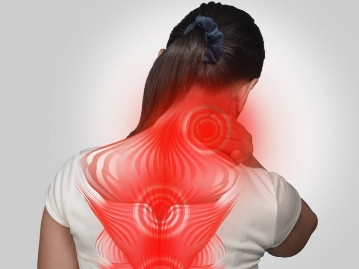 一个年轻女子面对从肌肉疼痛墙上的痛苦与她的手在她的脖子
