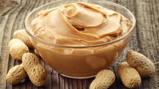 填充有花生酱的透明碗包围由原料干燥花生上的木桌