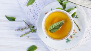 薄荷的叶子和茶在杯子在一张白色木桌上
