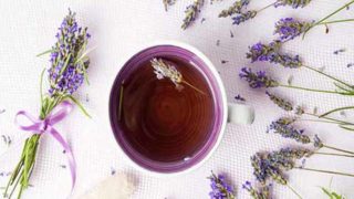 在一个杯子的紫色茶在有淡紫色花的一个白板围拢它
