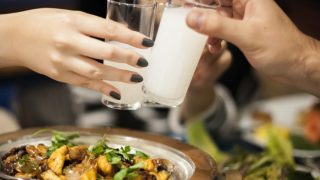 两只手在一碗食物上碰杯喝白酒。