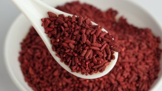一个勺子装满了红曲米的特写镜头,与一个朦胧的白色碗盛满红曲米的图片形成对比