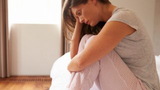 一个女人面色心疼,坐在她的睡衣在床上