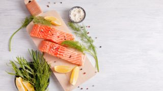 生三文鱼放在木板上,上面有柠檬片、莳萝、海盐和胡椒