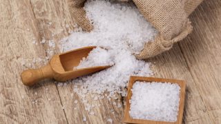 一袋海盐洒在桌子上,一个木勺子和一盘海盐放在一张木桌上