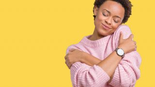 一个女人在黄色的背景下拥抱着自己,脸上挂着微笑