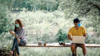 在长凳上戴着面具保持社交距离