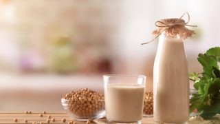 木桌上放着一碗大豆种子、一个玻璃杯和一罐豆浆