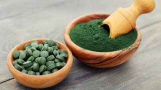 装有绿色螺旋藻粉和螺旋藻丸的木碗放在黑色的柜台上