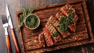 牛排、酱汁和几根草本植物的嫩枝,刀叉放在桌子上