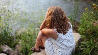 一位身穿圆点连衣裙、手放在前额的妇女,坐在一条小溪旁