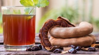 木桌上放着一杯罗望子汁和新鲜罗望子水果,有皮也有皮